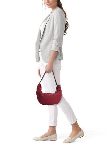 Bordeaux schoudertas van Calvin Klein, gedragen door een vrouw met een grijze blazer, witte broek en beige loafers.
