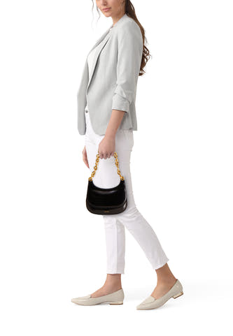 Sac à dos noir de Calvin Klein, avec une poignée en chaîne d'or, porté avec un blazer gris et un pantalon blanc.
