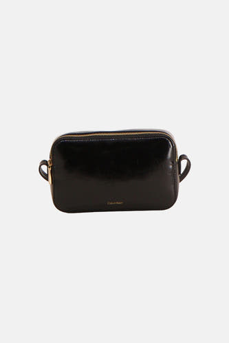 Zwarte schoudertas van Calvin Klein van glimmend materiaal met gouden ritssluiting en een goudkleurig logo op de voorkant.