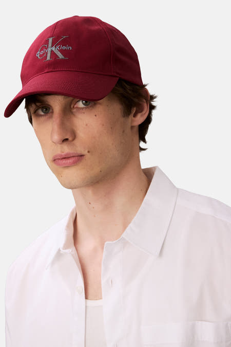 Rode pet van Calvin Klein, met logo borduursel op de voorkant, gedragen door een model met een wit overhemd.
