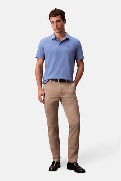 Man met blauw poloshirt, beige broek en zwarte loafers.