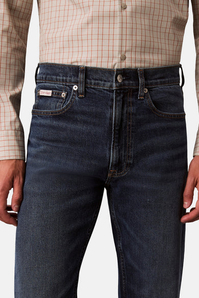Donkerblauwe straight jeans van Calvin Klein, met subtiele stiksels en een beige geruit overhemd.
