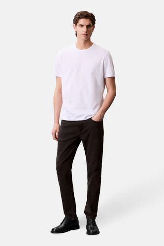 Jean tapered en denim gris foncé de Calvin Klein, porté avec un T-shirt blanc et des chaussures noires.
