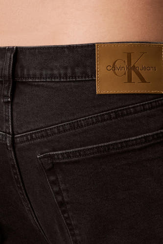 Boutons de fermeture éclair sur des jeans en denim gris foncé de Calvin Klein, avec un étiquette en cuir marron sur la ceinture.