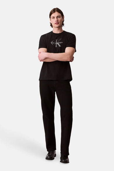 Zwart T-shirt met korte mouwen van Calvin Klein, gedragen met zwarte jeans en schoenen, met gekruiste armen.
