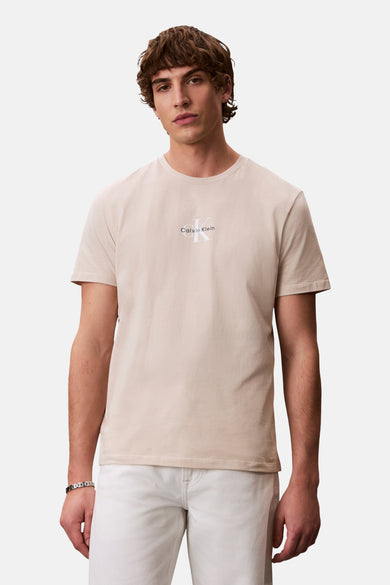 Ecrukleurig T-shirt met korte mouwen van Calvin Klein, gedragen met een witte broek en een zilveren armband.
