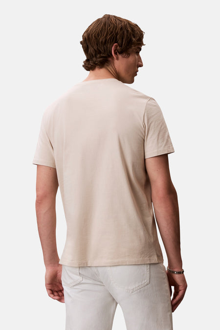 Ecru T-shirt met korte mouwen van Calvin Klein, rugaanzicht op een man, gecombineerd met een witte broek en een zilveren armband.
