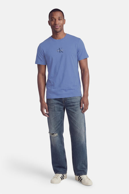 Blauwe korte mouw T-shirt van Calvin Klein met klein logo op borst, gedragen met versleten jeans en witte sneakers, front view