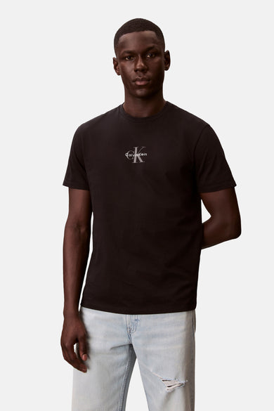 Zwart T-shirt met korte mouwen van Calvin Klein met zilverkleurig CK-logo op de borst, gedragen door model met lichtblauwe gescheurde jeans.