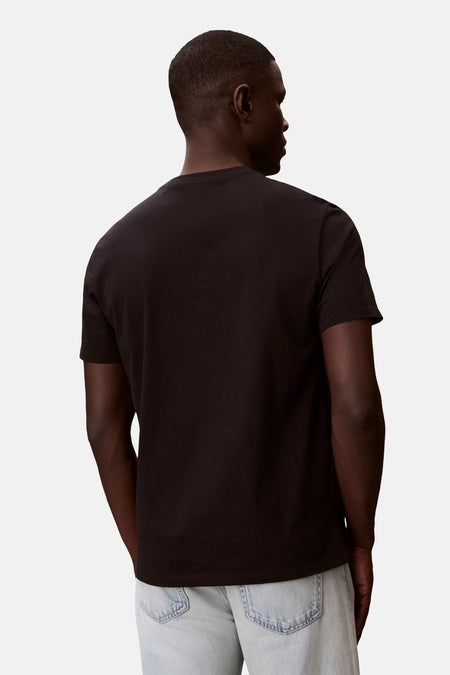 Zwart T-shirt met korte mouwen van Calvin Klein, gedragen door een model met de rug naar de camera en een lichte spijkerbroek.