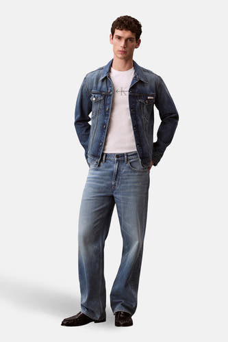 T-shirt blanc à manches courtes de Calvin Klein, porté sous une veste en denim avec des jeans coordonnés et des chaussures noires.