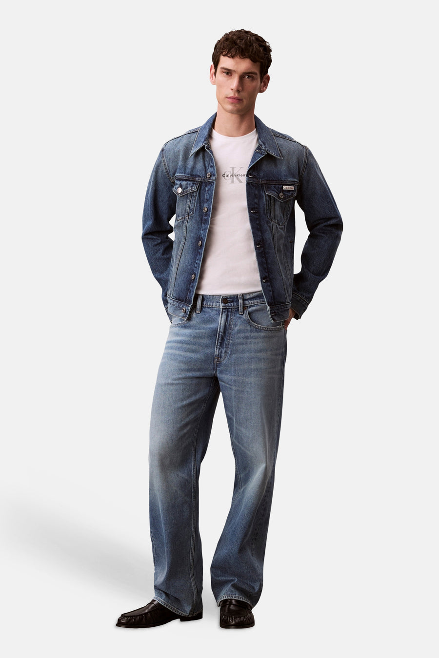 T-shirt blanc à manches courtes Calvin Klein, avec logo noir discret, combiné avec une veste en jean bleue, un jean et des mocassins noirs.