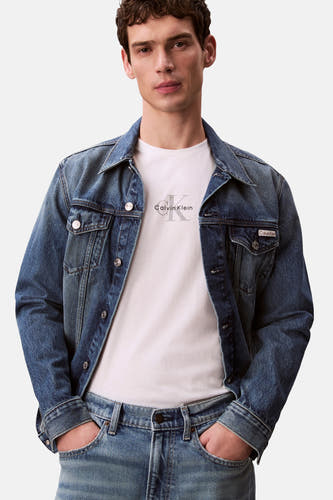 T-shirt blanc à manches courtes Calvin Klein avec logo sur la poitrine, porté par un homme en veste en jean et jean.