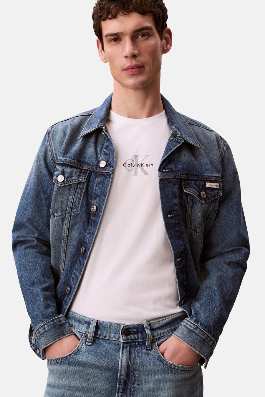 T-shirt blanc à manches courtes Calvin Klein avec logo sur la poitrine, porté par un homme en veste en jean et jean.
