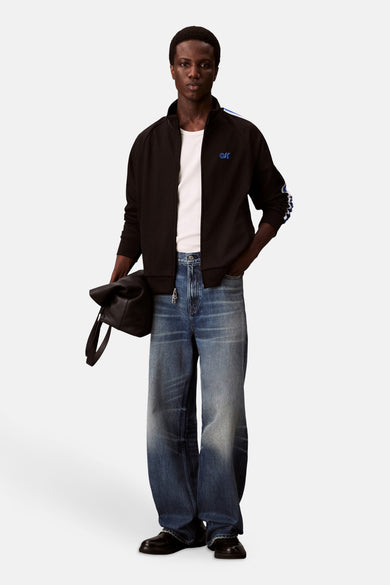 Zwarte sweater gilet van Calvin Klein, met witte strepen op de mouwen en een witte T-shirt onder de gilet.