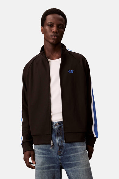Zwarte sweater van Calvin Klein met blauw-witte strepen op de mouwen, gedragen over een wit shirt en blauwe jeans.
