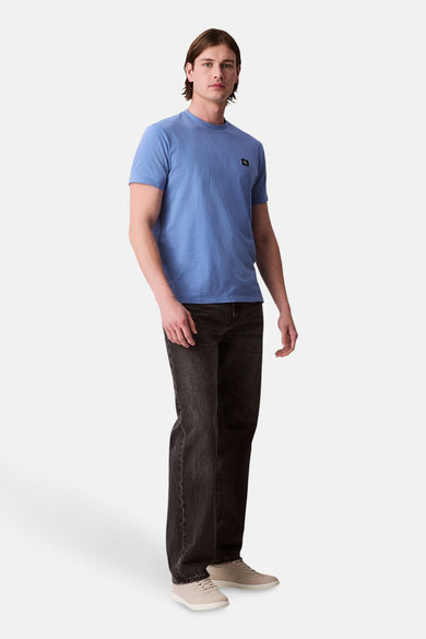T-shirt bleu à manches courtes de Calvin Klein, avec un petit logo sur la poitrine, associé à des jeans foncés et des baskets légères.