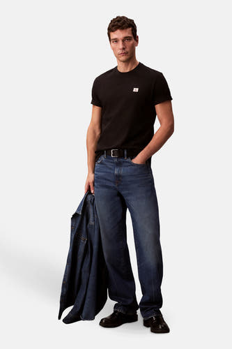 T-shirt noir à manches courtes de Calvin Klein, porté avec des jeans bleus et un blouson en denim.
