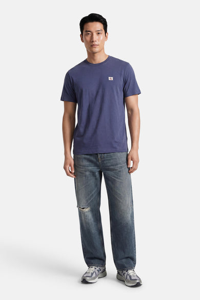 Blauwe korte mouw T-shirt van Calvin Klein met klein logo op borst, gedragen met versleten jeans en sneakers, front view