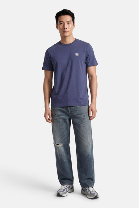 Blauwe korte mouw T-shirt van Calvin Klein met klein logo op borst, gedragen met versleten jeans en sneakers, front view