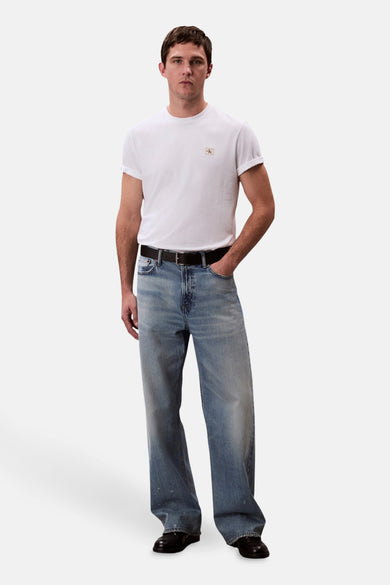 Wit T-shirt met korte mouwen van Calvin Klein, gedragen met wijde jeans en een zwarte leren riem.