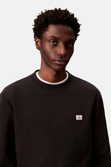 Zwarte sweater met ronde hals van Calvin Klein, met klein logo op de borst en witte kraag.

