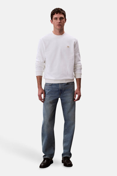 Pull-over blanc de Calvin Klein, vue de face, porté avec des jeans bleus et des chaussures noires.