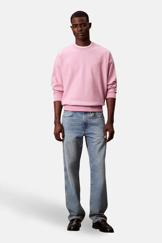 Roze sweater van Calvin Klein, met lange mouwen, gecombineerd met blauwe jeans en zwarte loafers.
