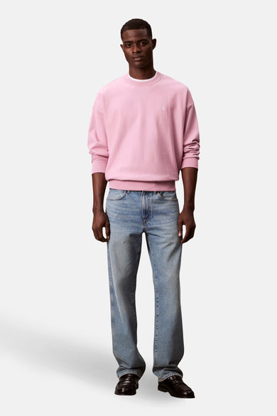 Gilet rose de Calvin Klein, avec des manches longues, associé à des jeans bleus et des loafers noirs.