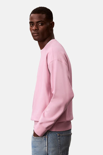 Roze sweater van Calvin Klein, met lange mouwen en een ronde hals, gedragen met jeans in zij-aanzicht.
