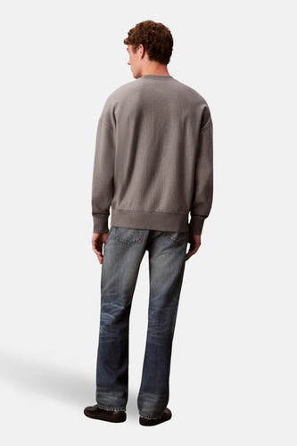 Grijze sweater van Calvin Klein, met lange mouwen en gedragen met blauwe jeans en zwarte schoenen, gezien van achteren.
