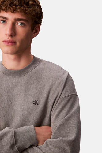 Grijze sweater van Calvin Klein, met een geborduurd 'cK'-logo en gekruiste armen.