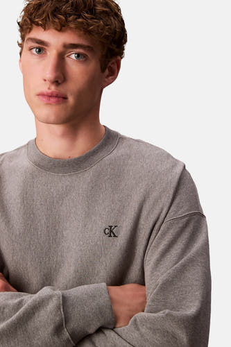 Grijze sweater van Calvin Klein, met klein zwart logo op de borst en gekruiste armen.