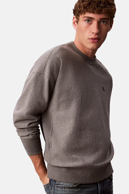 Grijze sweater van Calvin Klein met klein merklogo op de borst, gedragen met jeans.
