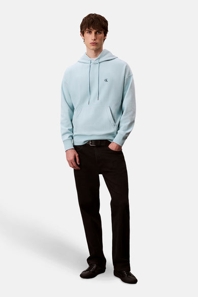 Sweat-shirt bleu avec capuche de Calvin Klein, doté d'un petit logo sur la poitrine, associé à des jeans noirs.