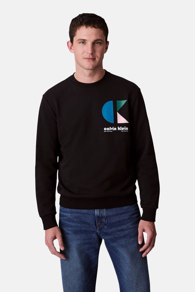 Zwarte sweater van Calvin Klein, met een grafisch logo op de borst en gedragen met een blauwe jeans.
