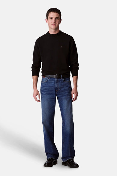 Pull-over noir de Calvin Klein, porté avec des jeans bleus à jambe droite et une ceinture en cuir noire.