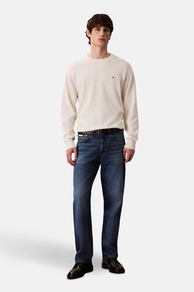 Gilet beige avec col rond de Calvin Klein, à longues manches, associé à des jeans bleus et des chaussures en cuir noires.