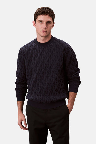 Pull-over bleu de Calvin Klein avec une texture imprimée, porté avec un pantalon noir en vue latérale.