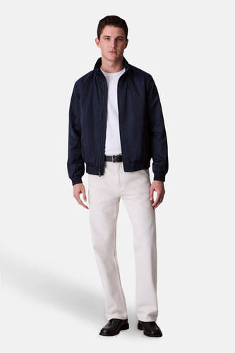 Blauwe regenjas van Calvin Klein, gedragen met een wit T-shirt, beige pantalon en zwarte leren schoenen.
