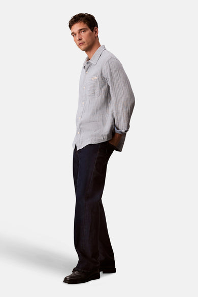 Chemise bleue à manches longues de Calvin Klein, avec une poche poitrine et portéeée des jeans noirs et des chaussures noires.