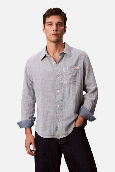 Chemise bleue rayée de Calvin Klein, à longues manches, avec poche poitrine et manches retroussées.