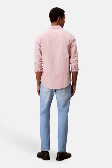 Slim fit jeans van lichtblauw denim van Calvin Klein, gezien van achteren, gecombineerd met een roze gestreept overhemd en zwarte schoenen.