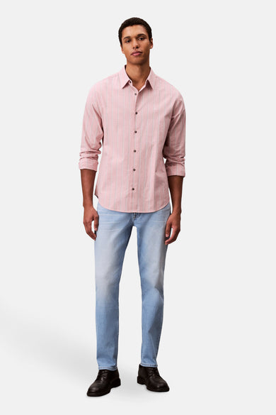 Slim jeans in lichtblauw denim van Calvin Klein, gecombineerd met een gestreept overhemd en zwarte schoenen.
