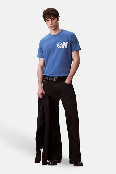 T-shirt bleu à manches courtes de Calvin Klein, porté avec des jeans noirs larges et un manteau.