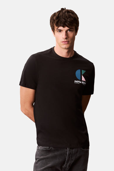 T-shirt noir à manches courtes de Calvin Klein, avec un logo graphique sur la poitrine et des jeans gris.