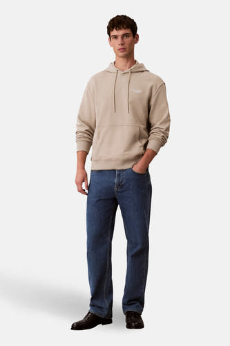 Pull-over beige avec capuchon de Calvin Klein, porté avec des jeans et des chaussures noires.