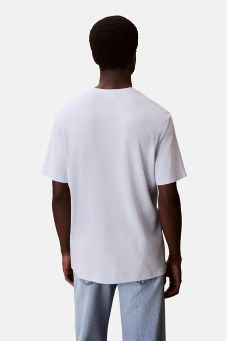 Blauw T-shirt met korte mouwen van Calvin Klein, achterkant zichtbaar, met een wafelpatroon, gedragen met een blauwe jeans.
