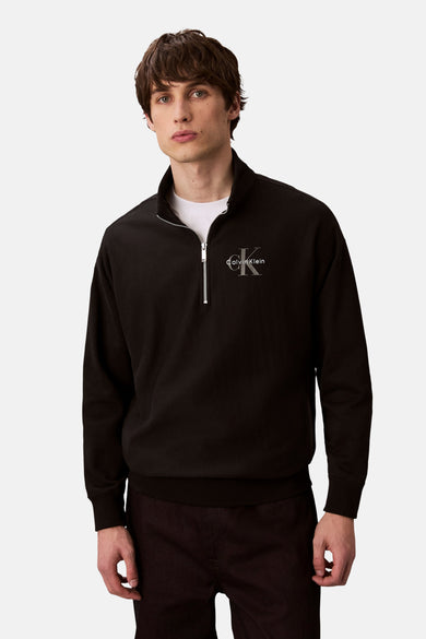 Pull-over noir avec fermeture à glissière de Calvin Klein, logo imprimé sur la poitrine, associé à un T-shirt blanc.