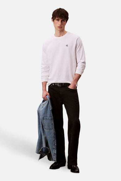 Wit T-shirt met lange mouwen van Calvin Klein, met een klein CK-logo op de borst, gedragen met zwarte jeans.

